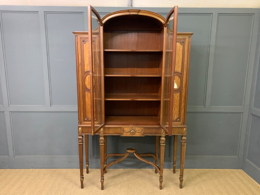 An antique mahogany display cabinet featuring glazed centre doors, side inlaid panels, fluted legs, and an arched top. View XIX