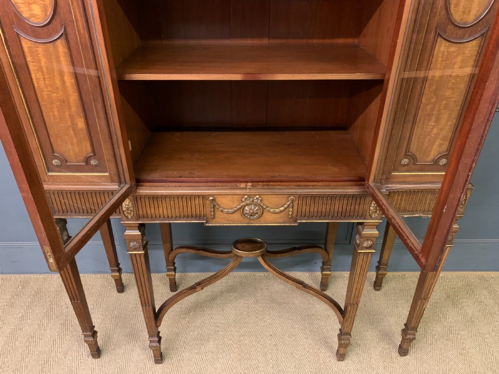 An antique mahogany display cabinet featuring glazed centre doors, side inlaid panels, fluted legs, and an arched top. View XX