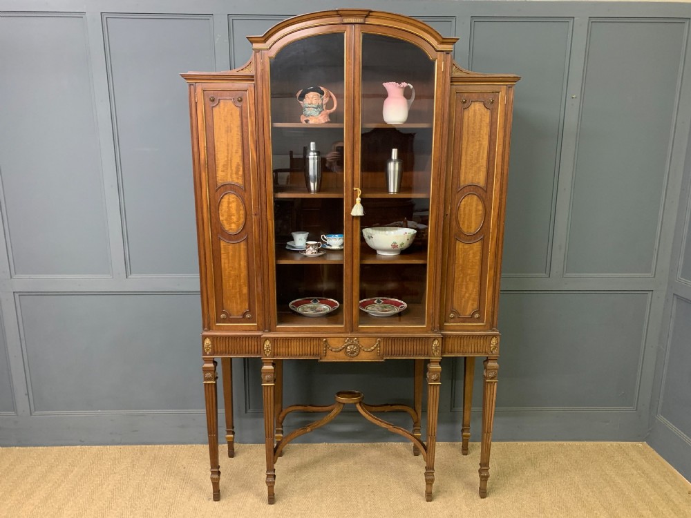 An antique mahogany display cabinet featuring glazed centre doors, side inlaid panels, fluted legs, and an arched top. View XXI
