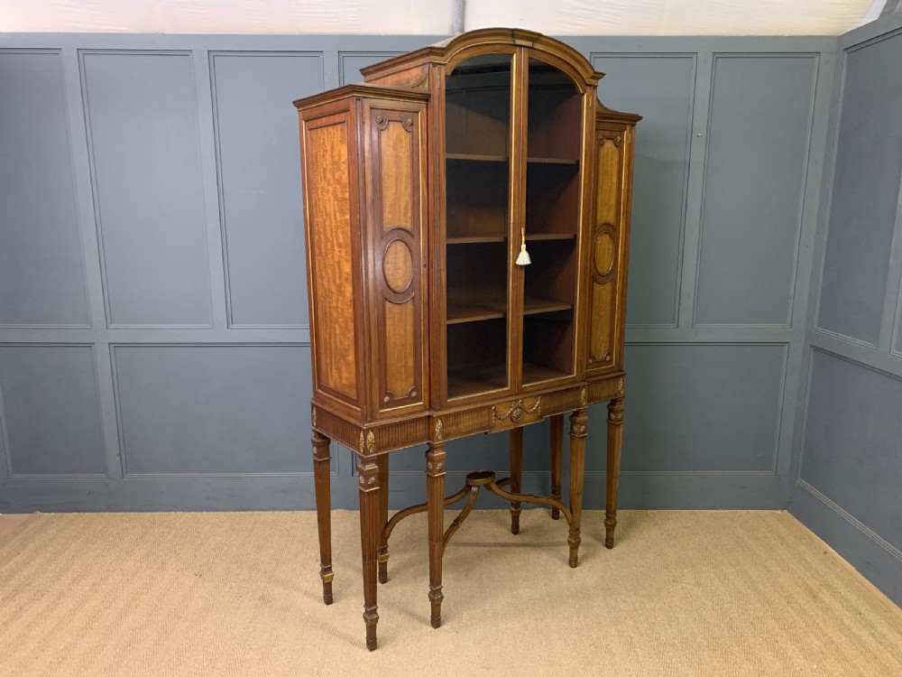 An antique mahogany display cabinet featuring glazed centre doors, side inlaid panels, fluted legs, and an arched top. View XXII
