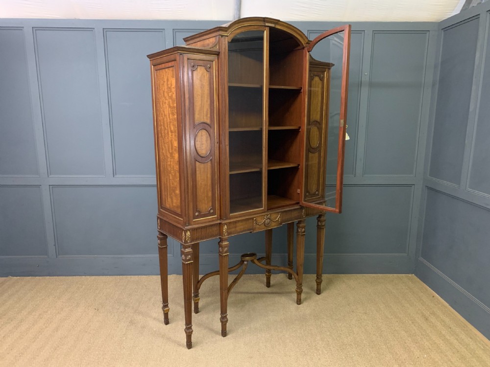 An antique mahogany display cabinet featuring glazed centre doors, side inlaid panels, fluted legs, and an arched top. View XXVI