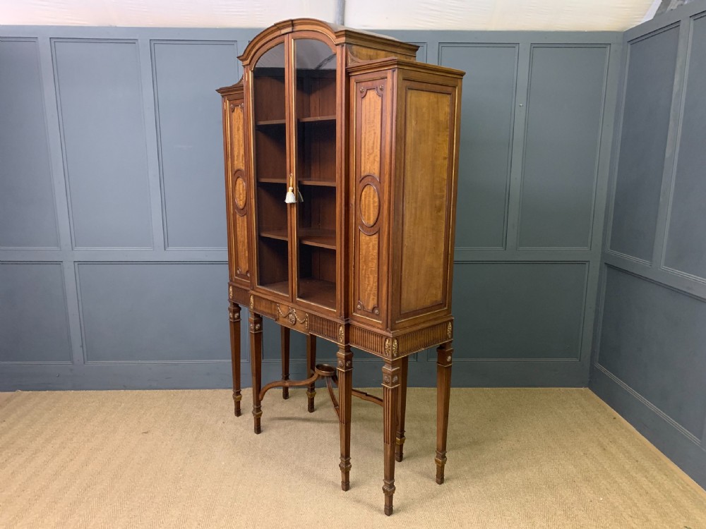 An antique mahogany display cabinet featuring glazed centre doors, side inlaid panels, fluted legs, and an arched top. View XXVII