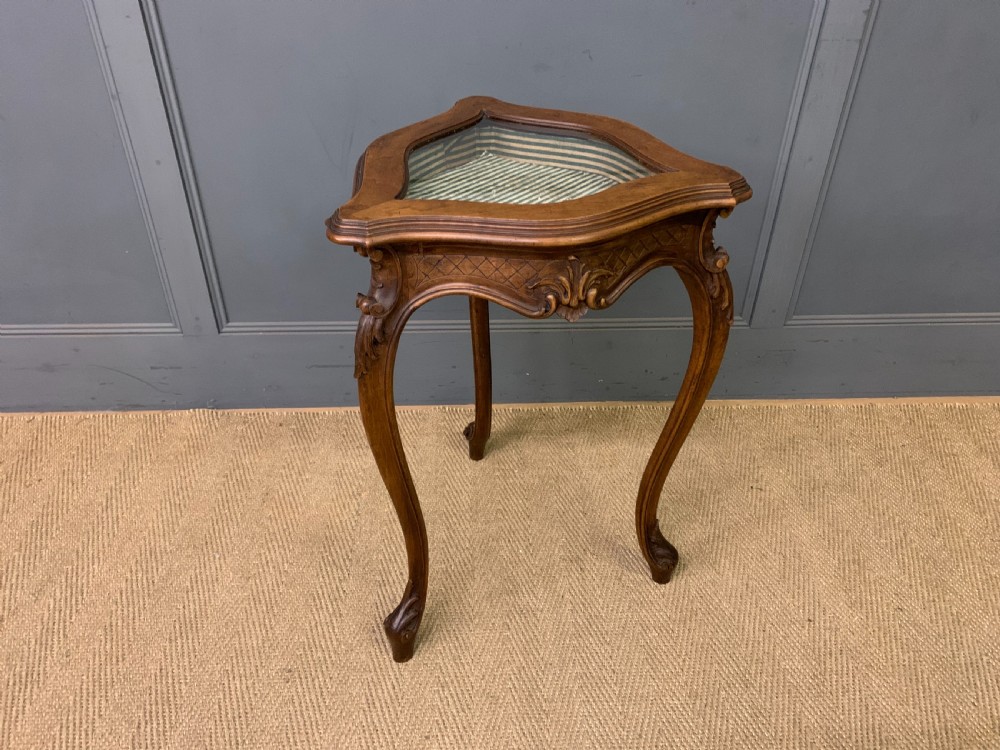 A French carved walnut bijouterie table featuring a trefoil-shaped hinged glass top, cabriole legs, and a striped fabric interior lining.