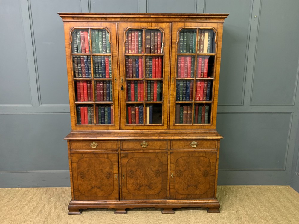 A large three-door burr walnut bookcase with glazed upper doors, three frieze drawers, and crossbanded cupboard doors below.