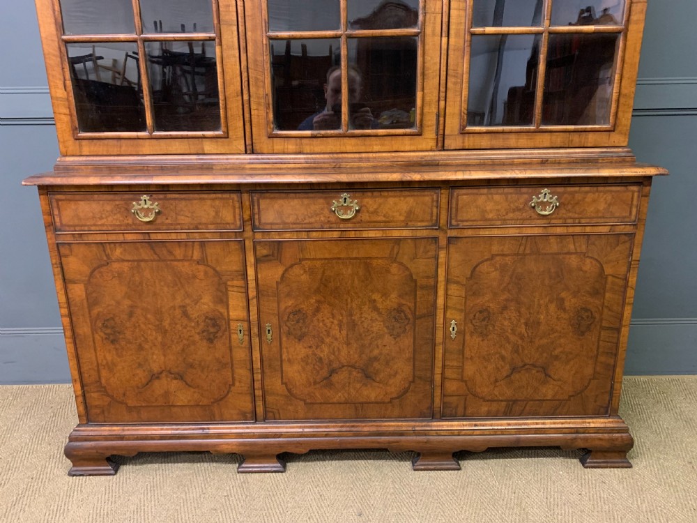 A large three-door burr walnut bookcase with glazed upper doors, three frieze drawers, and crossbanded cupboard doors below. View IV