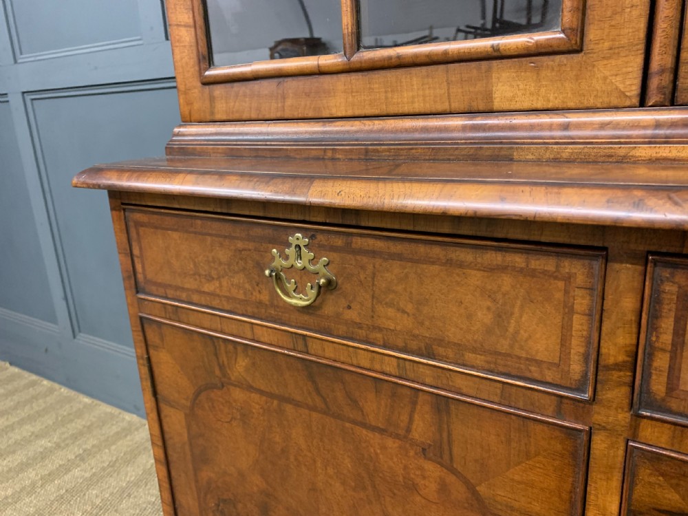 A large three-door burr walnut bookcase with glazed upper doors, three frieze drawers, and crossbanded cupboard doors below. View VII