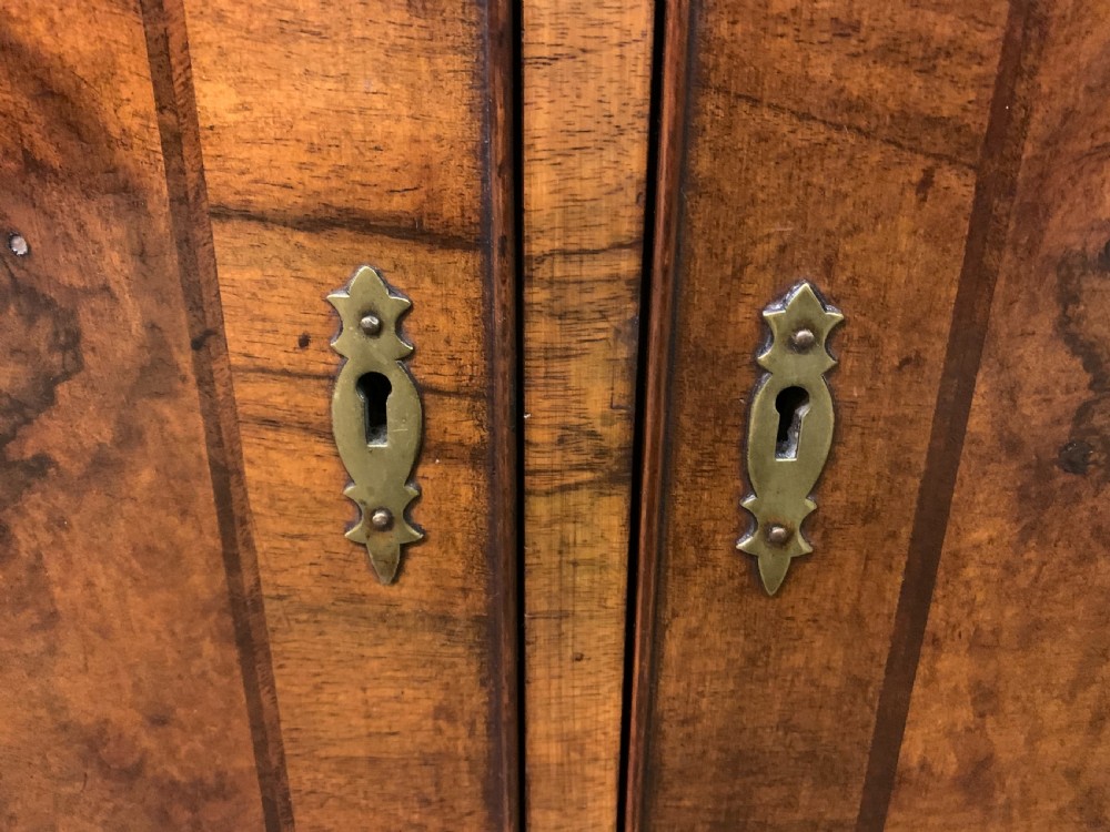 A large three-door burr walnut bookcase with glazed upper doors, three frieze drawers, and crossbanded cupboard doors below. View IX