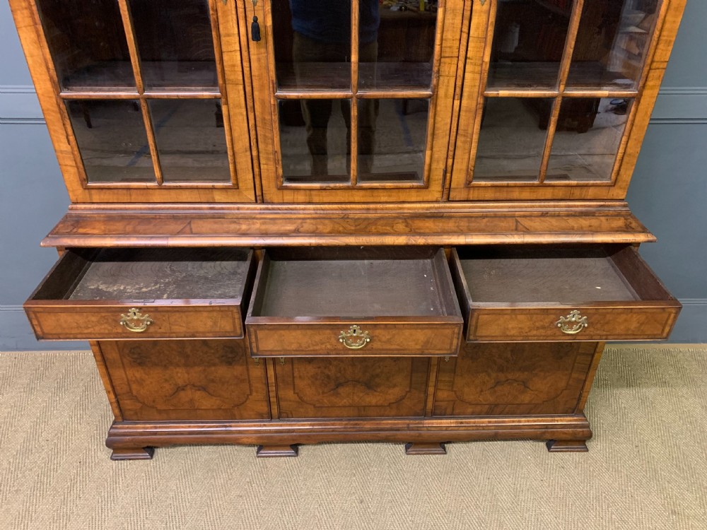 A large three-door burr walnut bookcase with glazed upper doors, three frieze drawers, and crossbanded cupboard doors below. View X