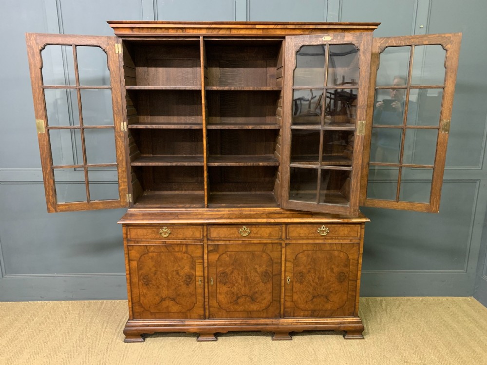 A large three-door burr walnut bookcase with glazed upper doors, three frieze drawers, and crossbanded cupboard doors below. View XV