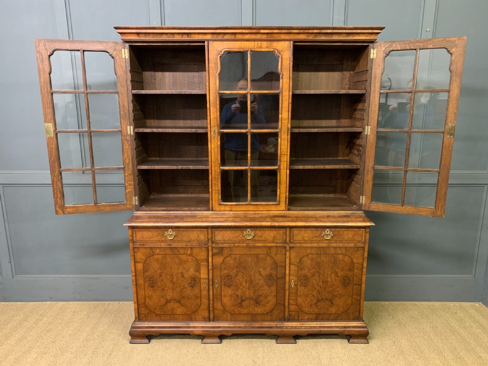 A large three-door burr walnut bookcase with glazed upper doors, three frieze drawers, and crossbanded cupboard doors below. View XVI