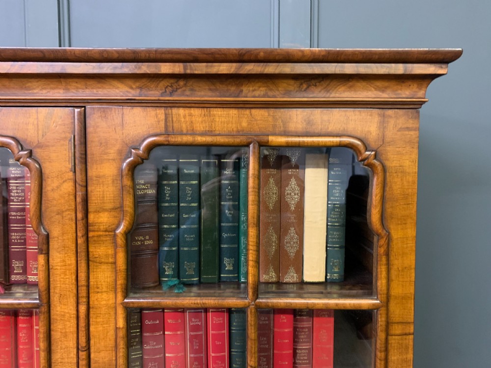 A large three-door burr walnut bookcase with glazed upper doors, three frieze drawers, and crossbanded cupboard doors below. View XX