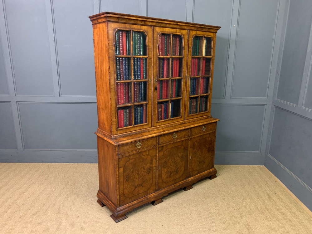A large three-door burr walnut bookcase with glazed upper doors, three frieze drawers, and crossbanded cupboard doors below. View XXI