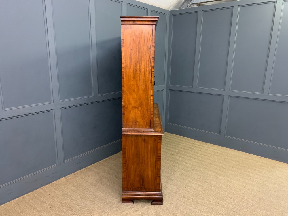 A large three-door burr walnut bookcase with glazed upper doors, three frieze drawers, and crossbanded cupboard doors below. View XXII