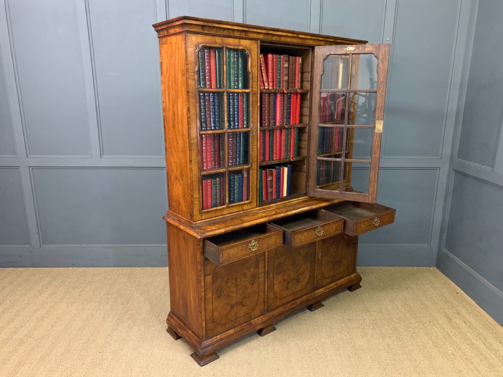 A large three-door burr walnut bookcase with glazed upper doors, three frieze drawers, and crossbanded cupboard doors below. View XXIV