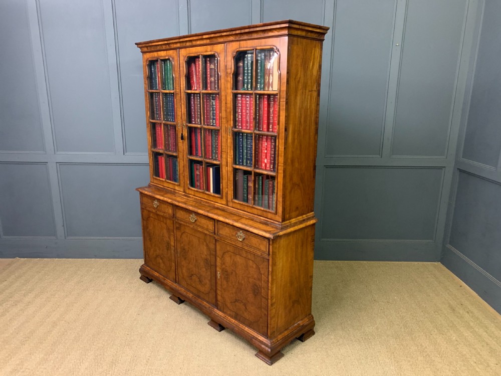 A large three-door burr walnut bookcase with glazed upper doors, three frieze drawers, and crossbanded cupboard doors below. View XXVI