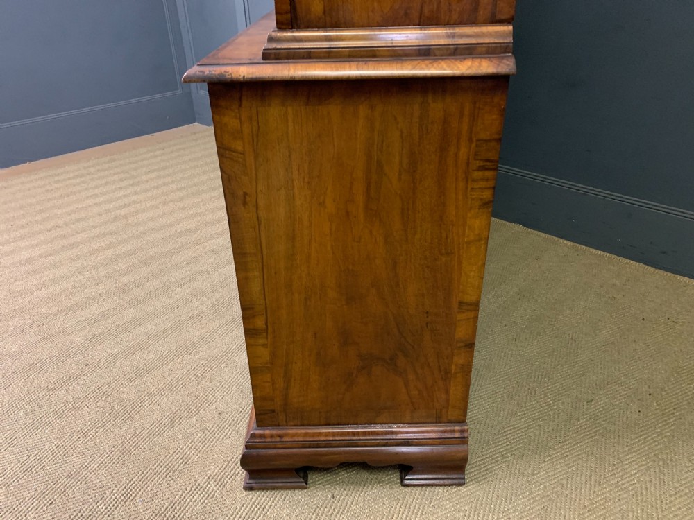 A large three-door burr walnut bookcase with glazed upper doors, three frieze drawers, and crossbanded cupboard doors below. View XXVII