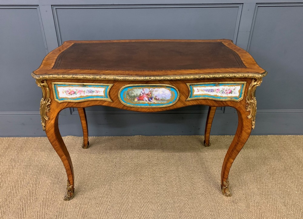 An antique Louis XV style French tulipwood bureau plat featuring a leather-inset top, gilt-bronze mounts, cabriole legs, and hand-painted porcelain plaques. View II