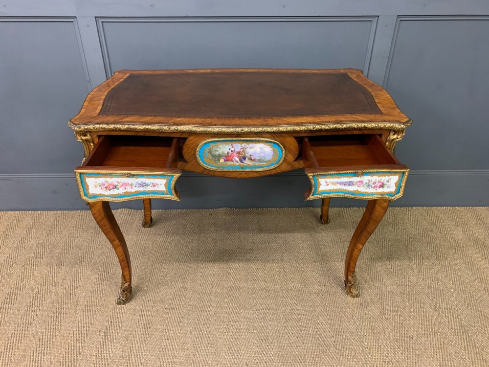 An antique Louis XV style French tulipwood bureau plat featuring a leather-inset top, gilt-bronze mounts, cabriole legs, and hand-painted porcelain plaques. View VII