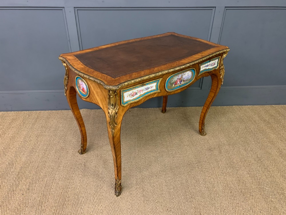 An antique Louis XV style French tulipwood bureau plat featuring a leather-inset top, gilt-bronze mounts, cabriole legs, and hand-painted porcelain plaques. View IX
