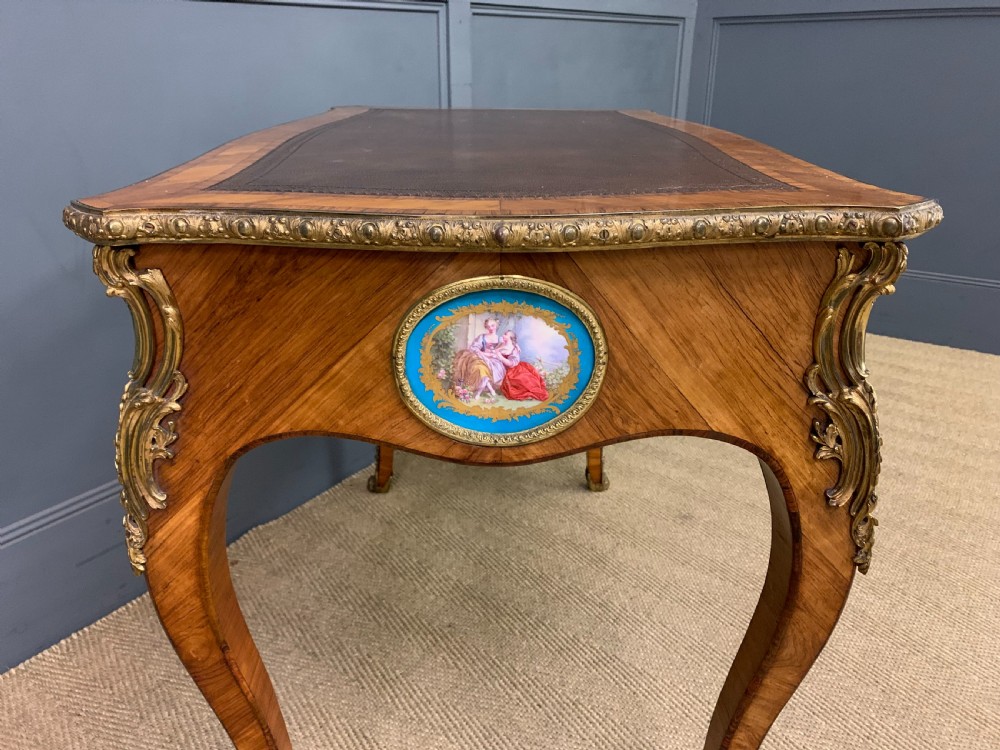 An antique Louis XV style French tulipwood bureau plat featuring a leather-inset top, gilt-bronze mounts, cabriole legs, and hand-painted porcelain plaques. View XI