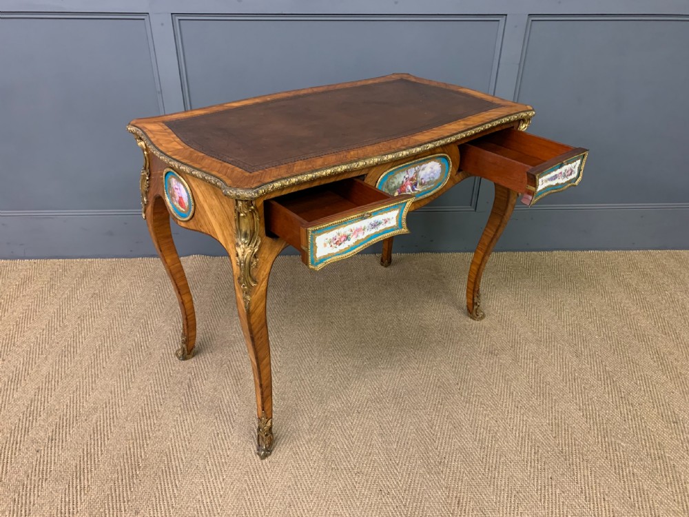 An antique Louis XV style French tulipwood bureau plat featuring a leather-inset top, gilt-bronze mounts, cabriole legs, and hand-painted porcelain plaques. View XVI
