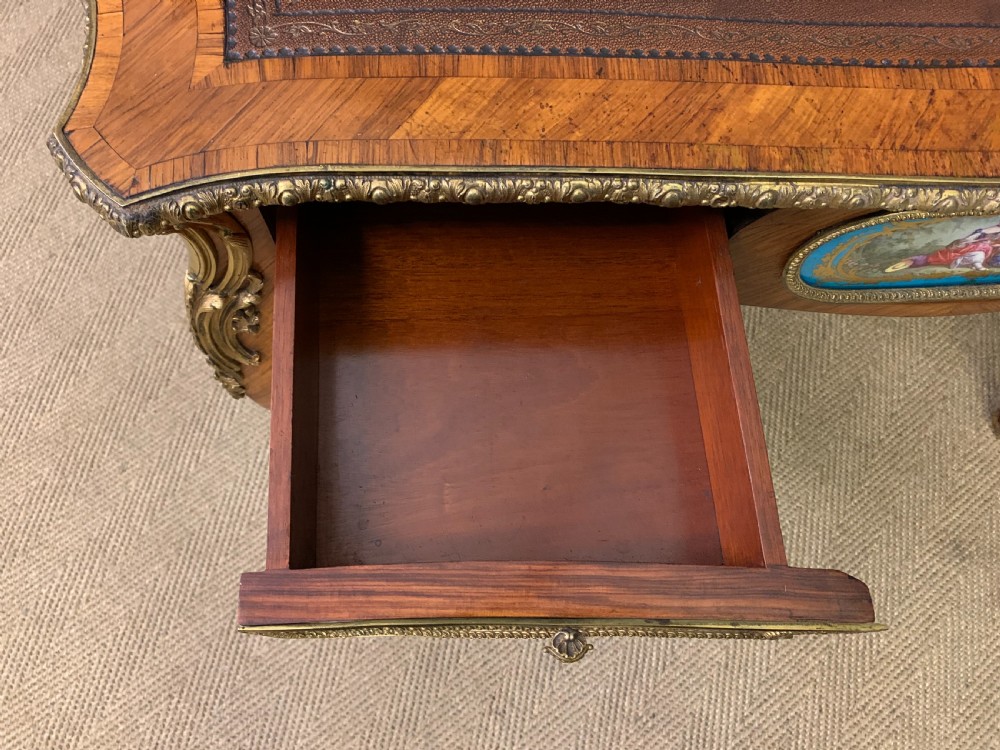 An antique Louis XV style French tulipwood bureau plat featuring a leather-inset top, gilt-bronze mounts, cabriole legs, and hand-painted porcelain plaques. View XVII