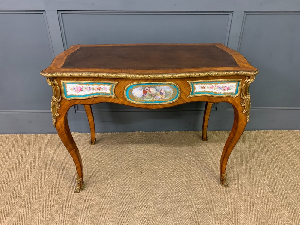An antique Louis XV style French tulipwood bureau plat featuring a leather-inset top, gilt-bronze mounts, cabriole legs, and hand-painted porcelain plaques. View XX