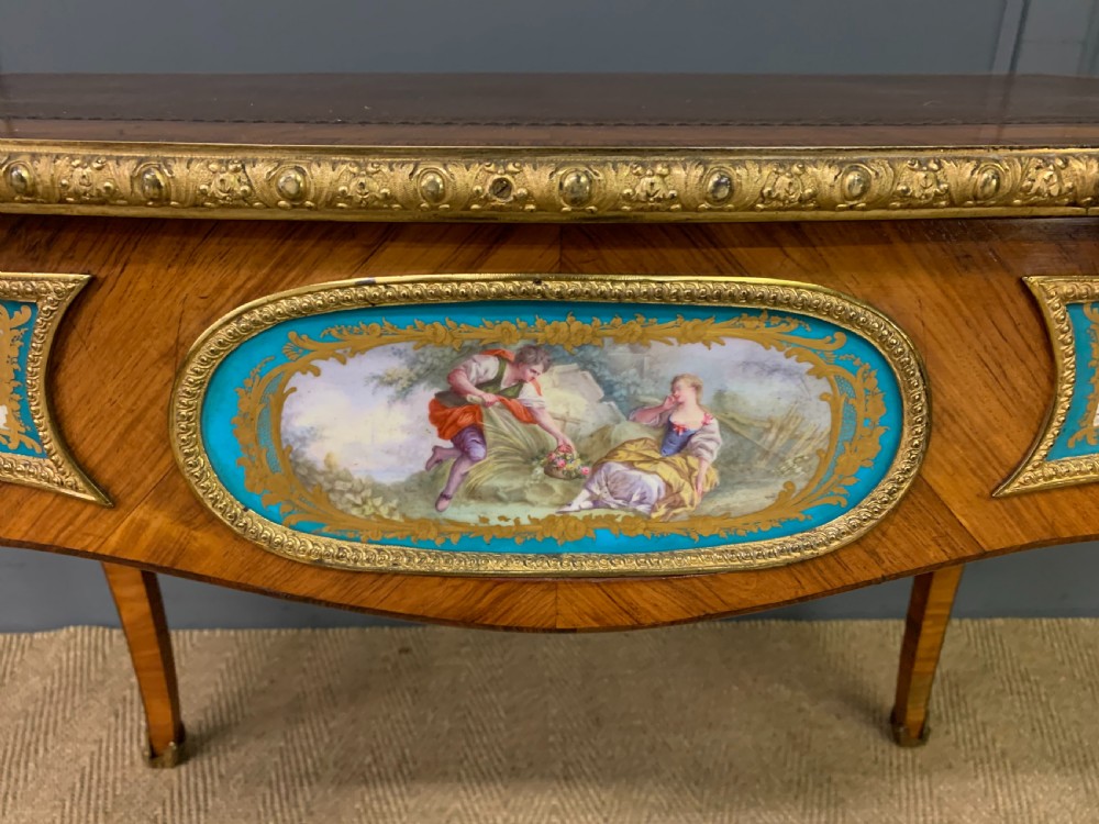 An antique Louis XV style French tulipwood bureau plat featuring a leather-inset top, gilt-bronze mounts, cabriole legs, and hand-painted porcelain plaques. View XXI