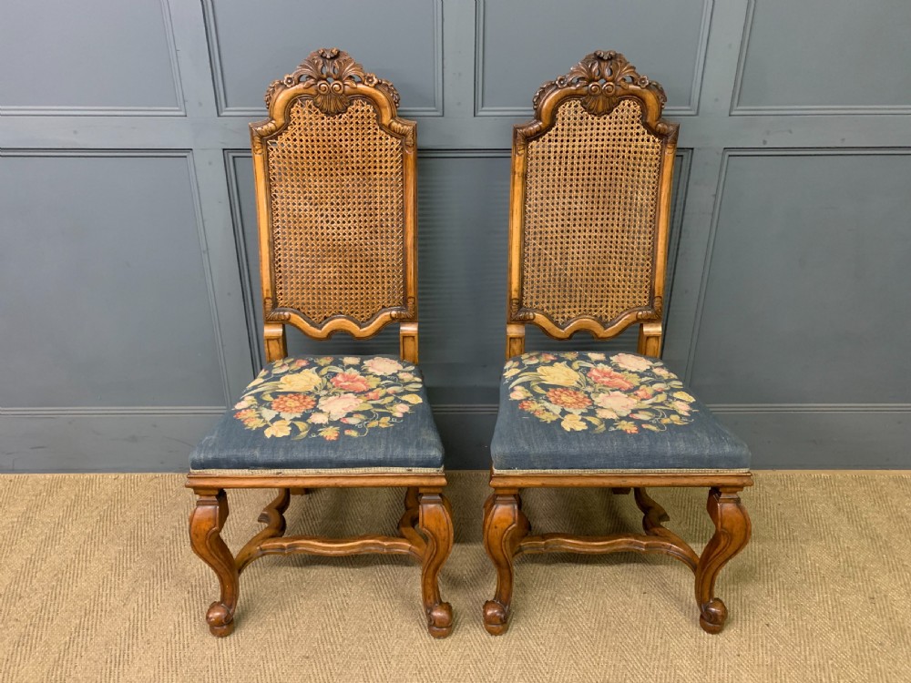 A pair of carved walnut side chairs with tall woven cane backs, floral tapestry upholstered seats, and scroll legs.