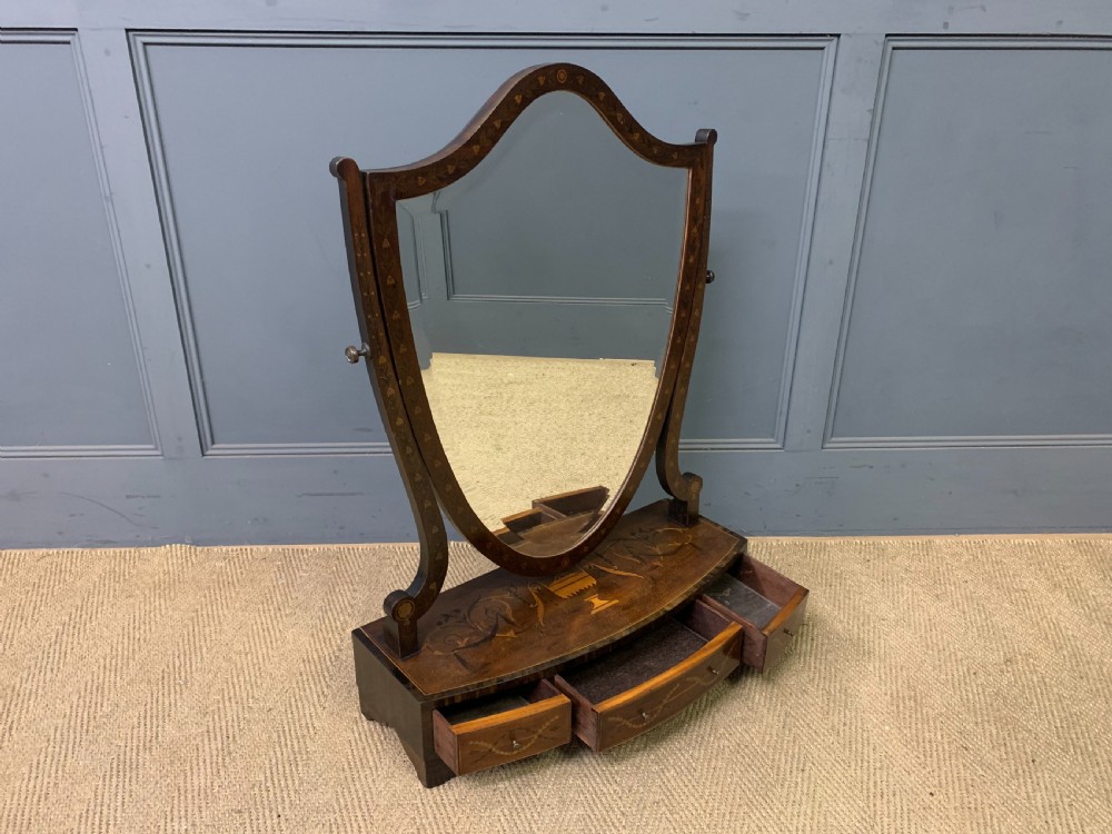 A Georgian mahogany toilet mirror featuring a shield-shaped swing frame, inlaid satinwood urn motifs, and a drawer base with curved fronting. View X