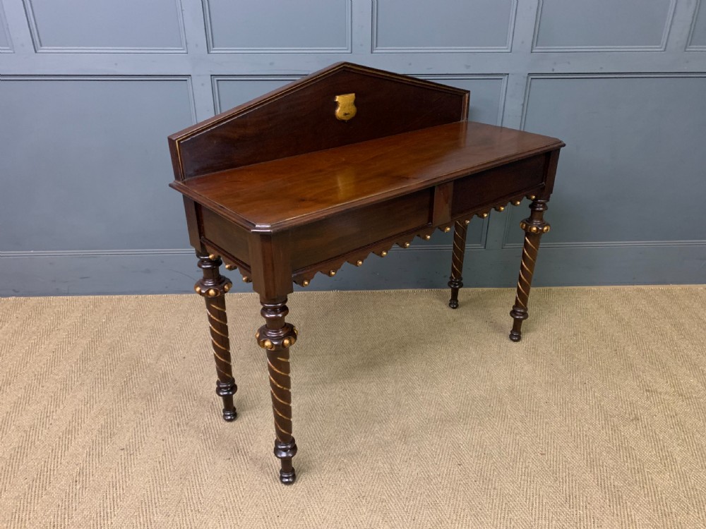 A dark mahogany Victorian hall table featuring spiral turned legs with gold accents, a scalloped apron, and an elevated gallery back with a central brass crest.
