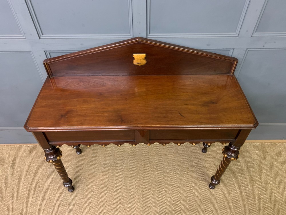 A dark mahogany Victorian hall table featuring spiral turned legs with gold accents, a scalloped apron, and an elevated gallery back with a central brass crest. View V