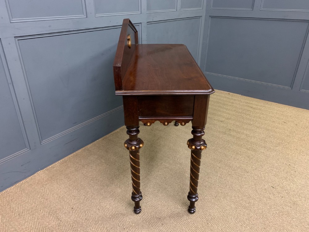 A dark mahogany Victorian hall table featuring spiral turned legs with gold accents, a scalloped apron, and an elevated gallery back with a central brass crest. View XI