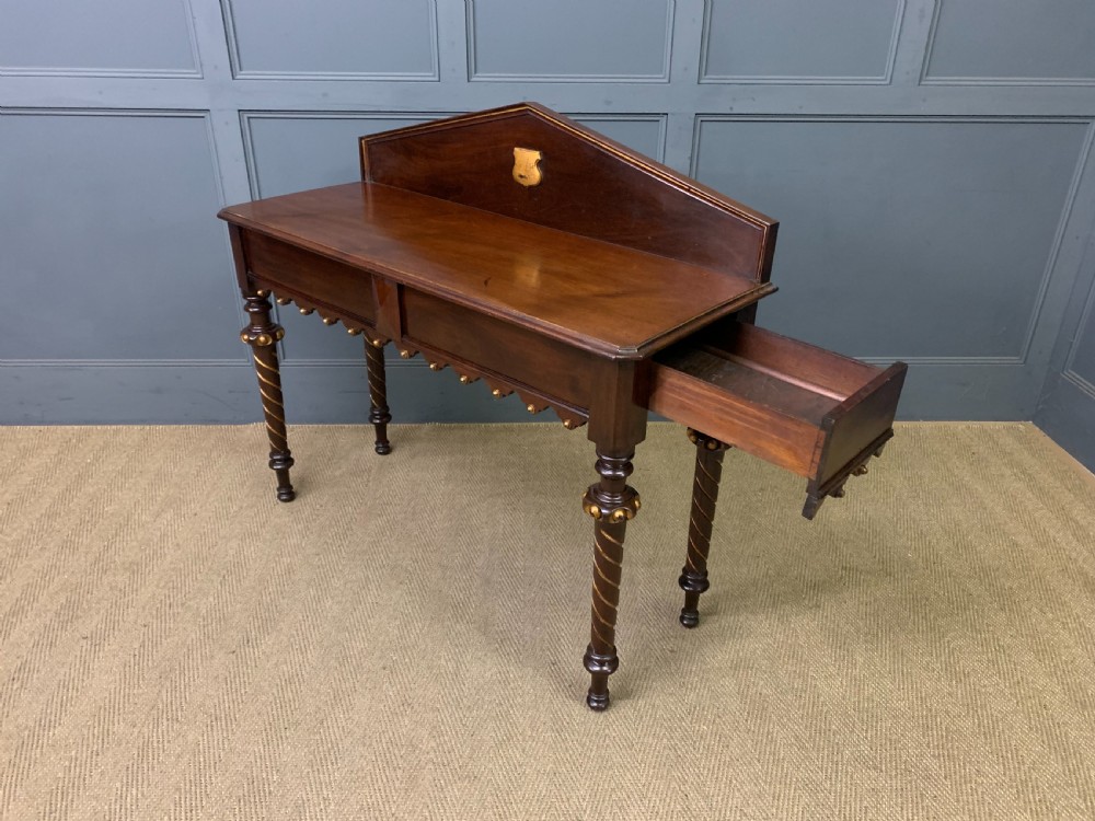 A dark mahogany Victorian hall table featuring spiral turned legs with gold accents, a scalloped apron, and an elevated gallery back with a central brass crest. View XVI