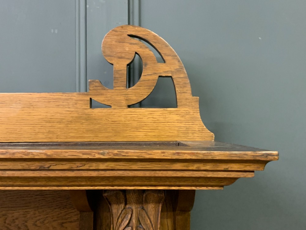 An Arts and Crafts golden oak sideboard featuring a mirrored superstructure with carved fretwork and blue ceramic cabochons above two drawers and two cupboard doors. View VIII