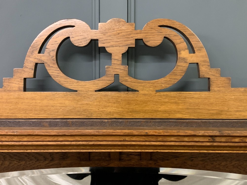 An Arts and Crafts golden oak sideboard featuring a mirrored superstructure with carved fretwork and blue ceramic cabochons above two drawers and two cupboard doors. View X