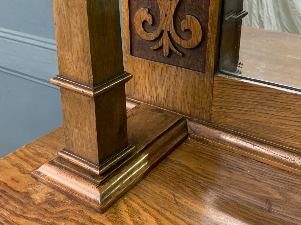 An Arts and Crafts golden oak sideboard featuring a mirrored superstructure with carved fretwork and blue ceramic cabochons above two drawers and two cupboard doors. View XI