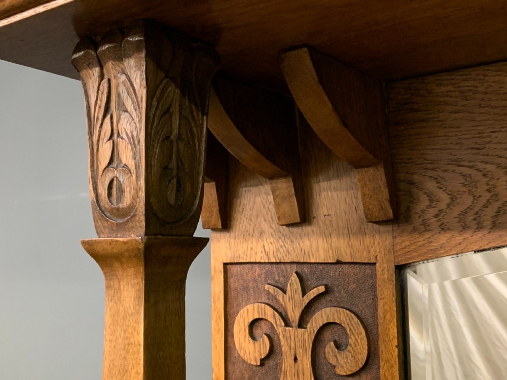 An Arts and Crafts golden oak sideboard featuring a mirrored superstructure with carved fretwork and blue ceramic cabochons above two drawers and two cupboard doors. View XIV