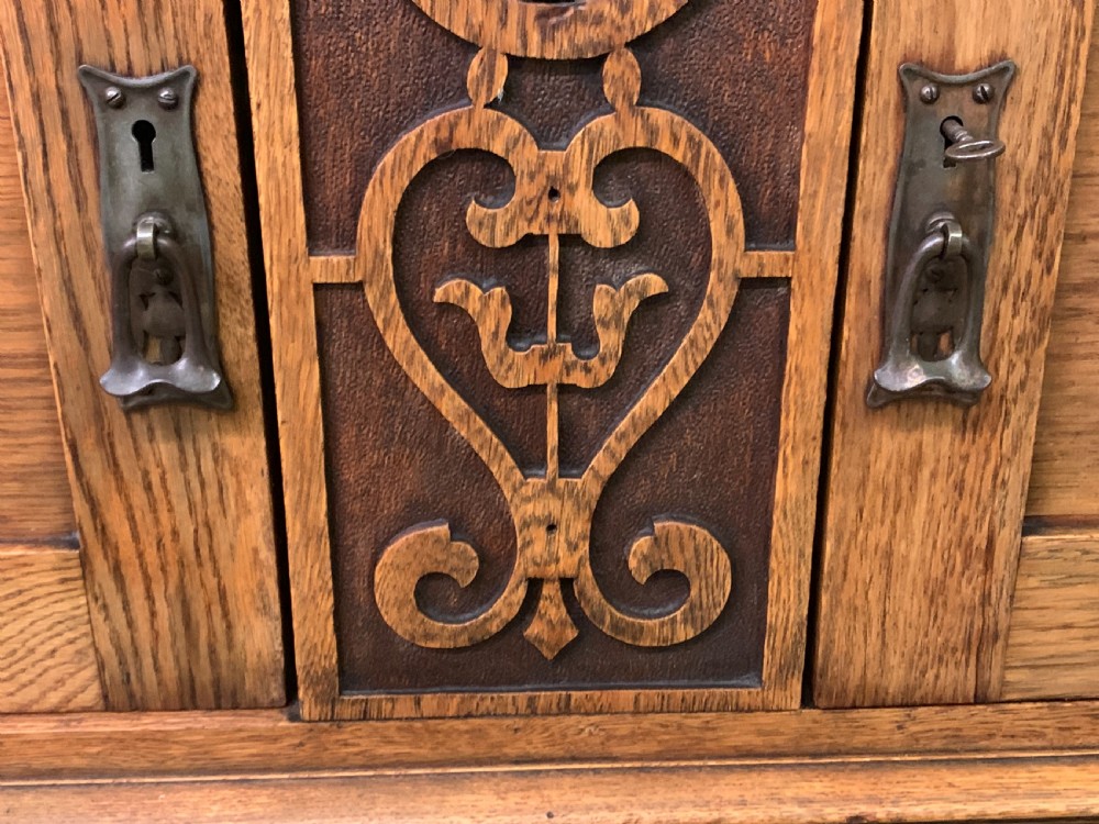 An Arts and Crafts golden oak sideboard featuring a mirrored superstructure with carved fretwork and blue ceramic cabochons above two drawers and two cupboard doors. View XVII