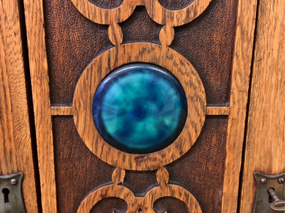 An Arts and Crafts golden oak sideboard featuring a mirrored superstructure with carved fretwork and blue ceramic cabochons above two drawers and two cupboard doors. View XVIII