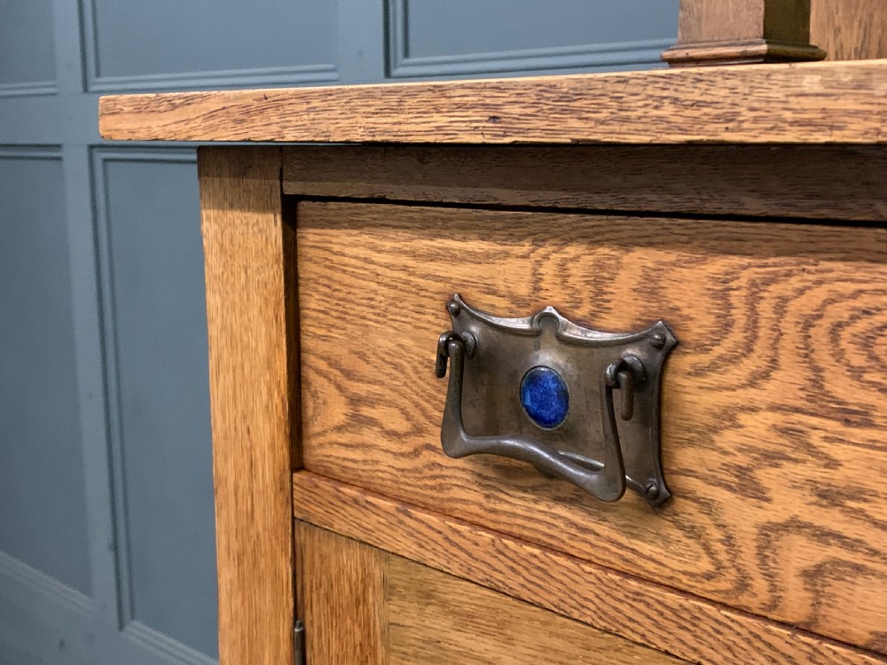 An Arts and Crafts golden oak sideboard featuring a mirrored superstructure with carved fretwork and blue ceramic cabochons above two drawers and two cupboard doors. View XIX