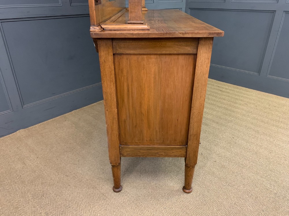 An Arts and Crafts golden oak sideboard featuring a mirrored superstructure with carved fretwork and blue ceramic cabochons above two drawers and two cupboard doors. View XXIV