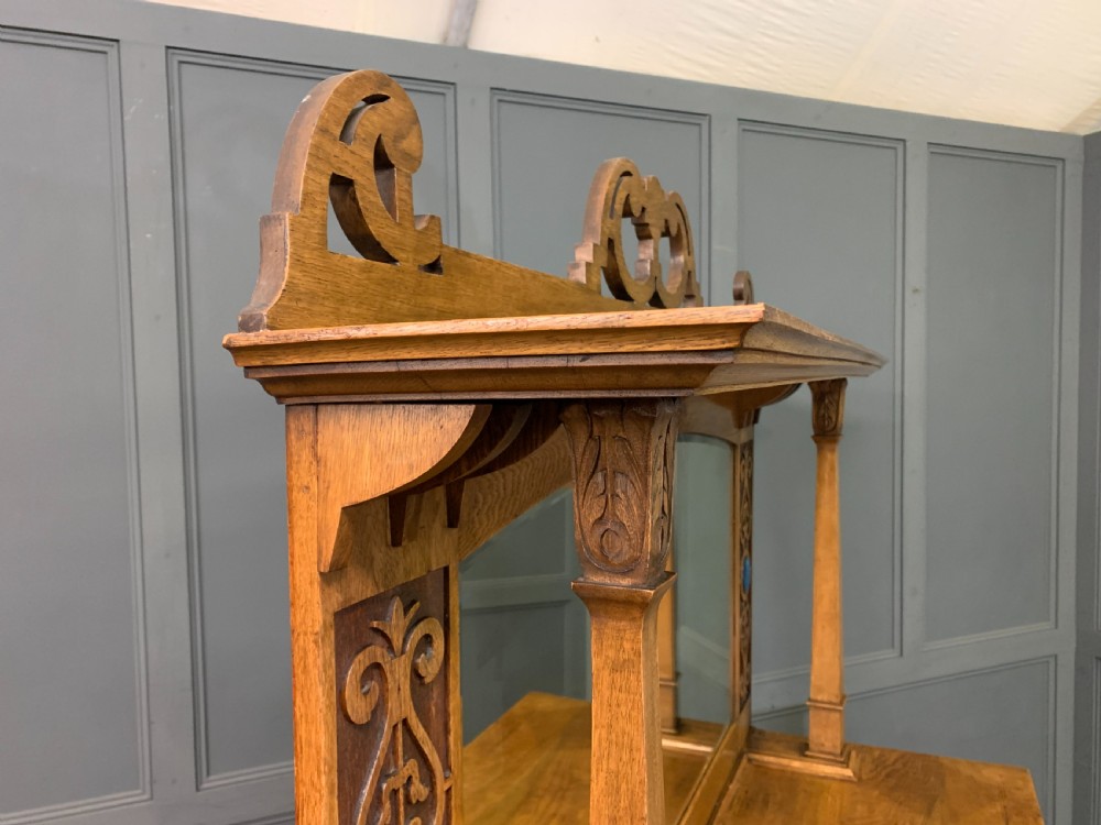 An Arts and Crafts golden oak sideboard featuring a mirrored superstructure with carved fretwork and blue ceramic cabochons above two drawers and two cupboard doors. View XXV