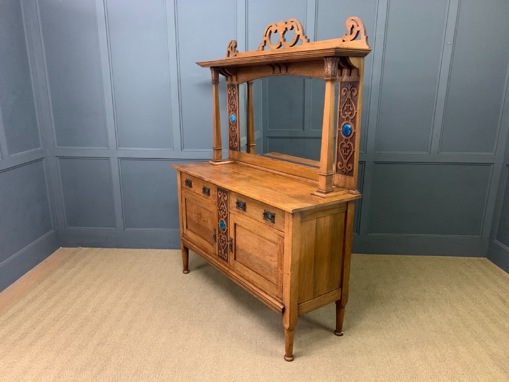 An Arts and Crafts golden oak sideboard featuring a mirrored superstructure with carved fretwork and blue ceramic cabochons above two drawers and two cupboard doors. View XXVIII