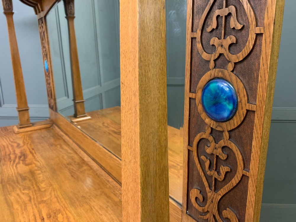An Arts and Crafts golden oak sideboard featuring a mirrored superstructure with carved fretwork and blue ceramic cabochons above two drawers and two cupboard doors. View XXIX