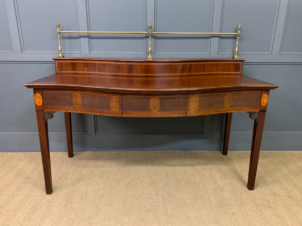 A George III mahogany serving table featuring a serpentine front, inlaid fluted detailing, square tapered legs, and a brass gallery rail. View II