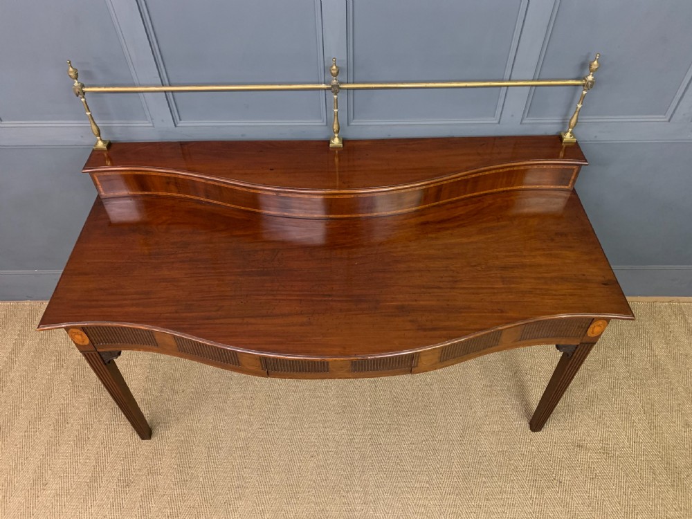 A George III mahogany serving table featuring a serpentine front, inlaid fluted detailing, square tapered legs, and a brass gallery rail. View III