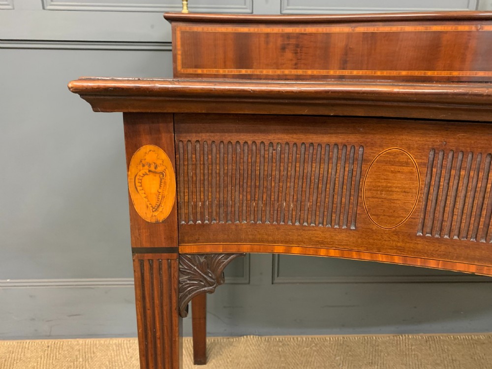 A George III mahogany serving table featuring a serpentine front, inlaid fluted detailing, square tapered legs, and a brass gallery rail. View IV