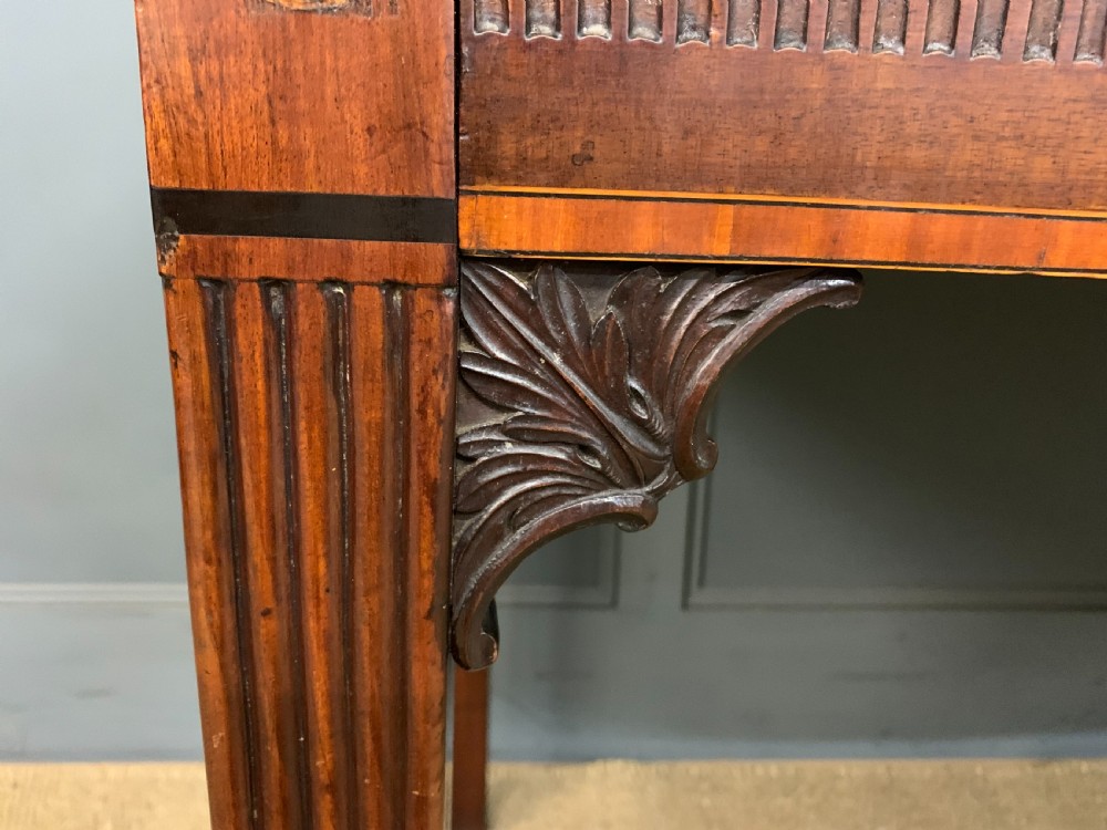 A George III mahogany serving table featuring a serpentine front, inlaid fluted detailing, square tapered legs, and a brass gallery rail. View VI