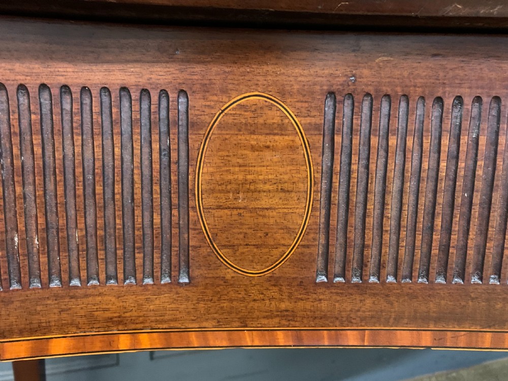 A George III mahogany serving table featuring a serpentine front, inlaid fluted detailing, square tapered legs, and a brass gallery rail. View VII